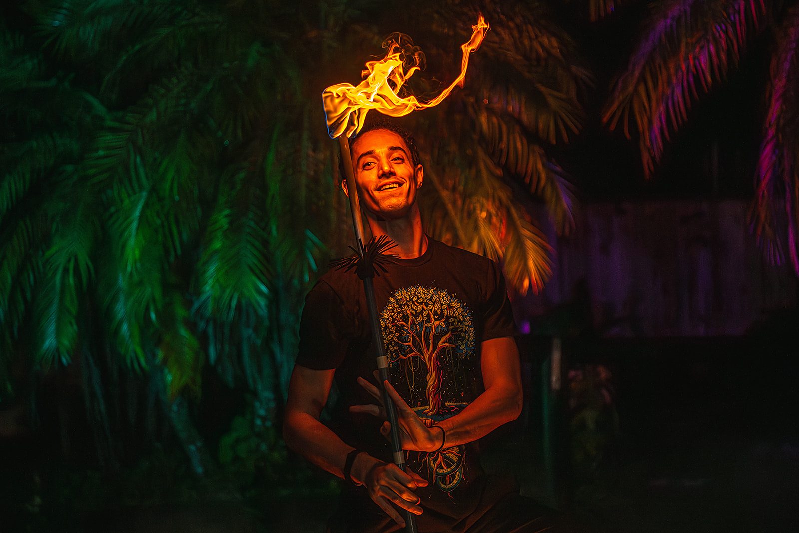 Portrait of Jake Jackson holding a fire staff upright, the flame curling above his head, wearing a tree-of-life shirt